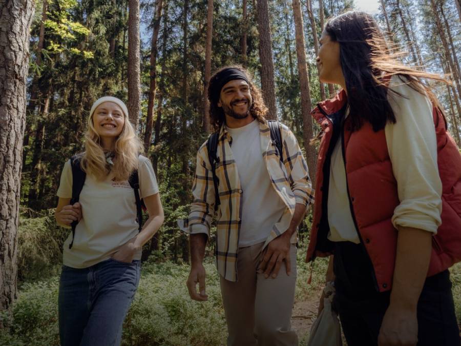 Tre escursionisti sorridenti in abiti casual da trekking autunnale nella foresta soleggiata