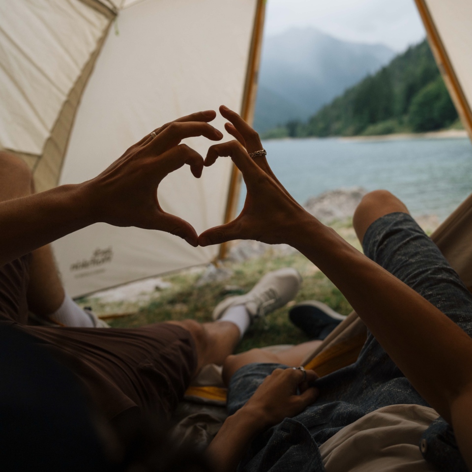 Due persone sdraiate in una tenda che unendo le loro mani formano un cuore